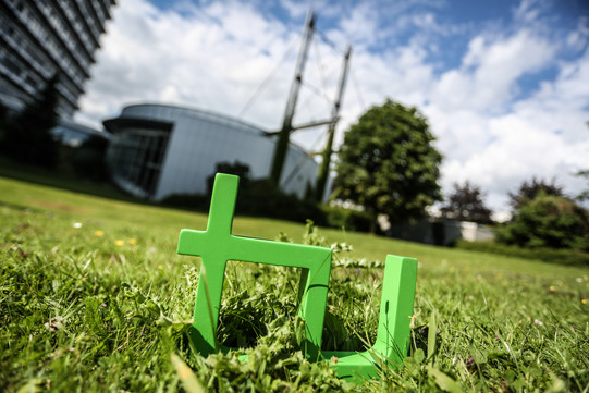 Im Vordergrund steht das TU-Logo im Gras, im Hintergrund das Audimax.